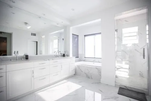 All-white master bathroom in marble with a double vanity, soaking tub and glass shower